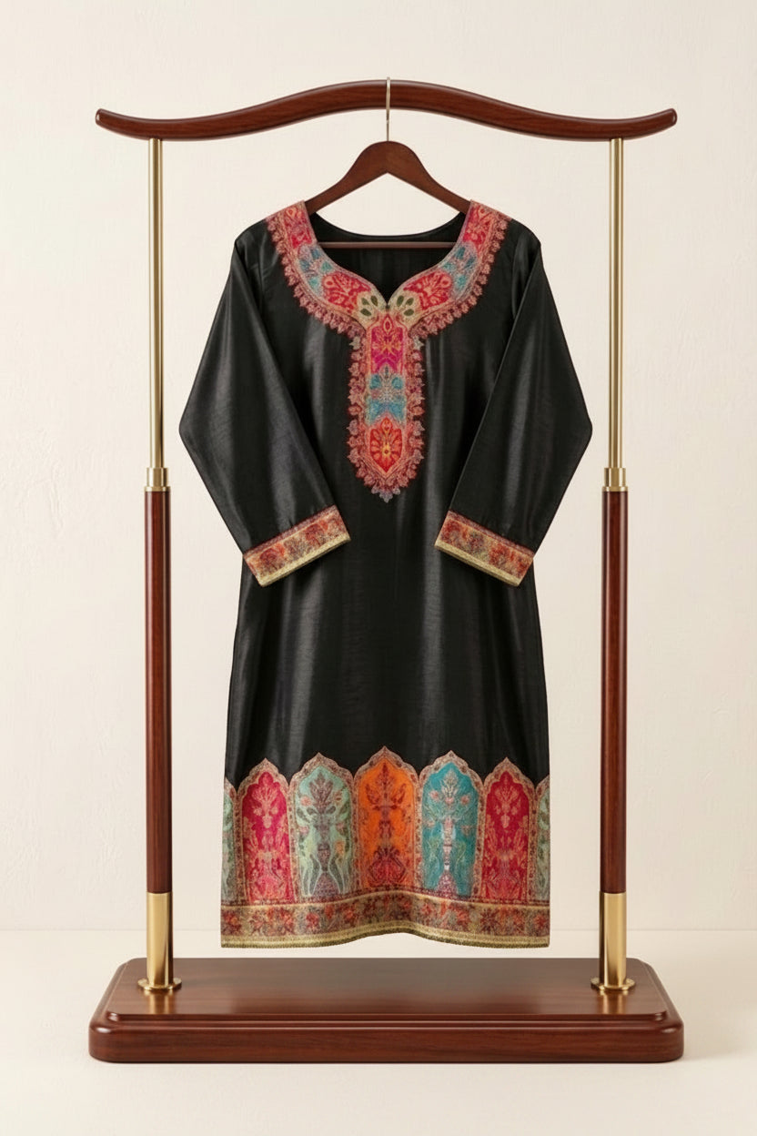 Front view of premium black silk kurta featuring intricate multicolored Kanni embroidery on neckline, sleeves and hem, enhanced with fine Zari detailing; displayed on an elegant wooden and gold stand against a soft neutral background, showcasing rich traditional craftsmanship and vibrant motifs.