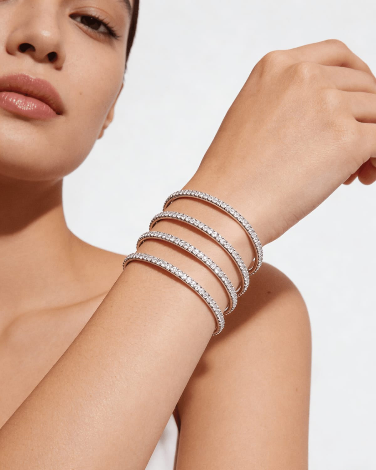 Woman wearing multiple silver bracelets on a plain background