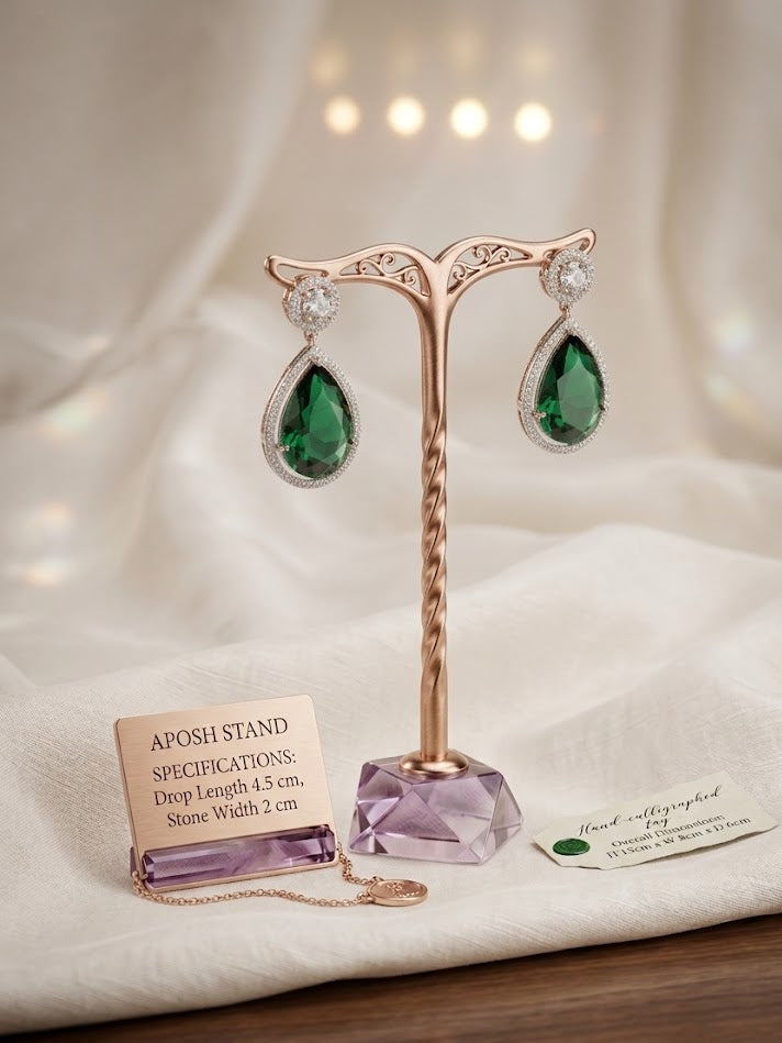 A posh brand jewelry display stand in rose gold featuring an amethyst base, showcasing a pair of emerald teardrop earrings with a 4.5 cm drop length.