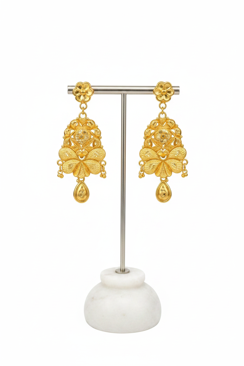 A pair of ornate gold-toned dangle earrings displayed on a silver metal stand with a white marble base against a plain white background.