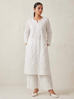 Woman standing wearing an elegant white mix cotton Chikankari kurta and matching plazo set with traditional Ghasspati hand-embroidery.