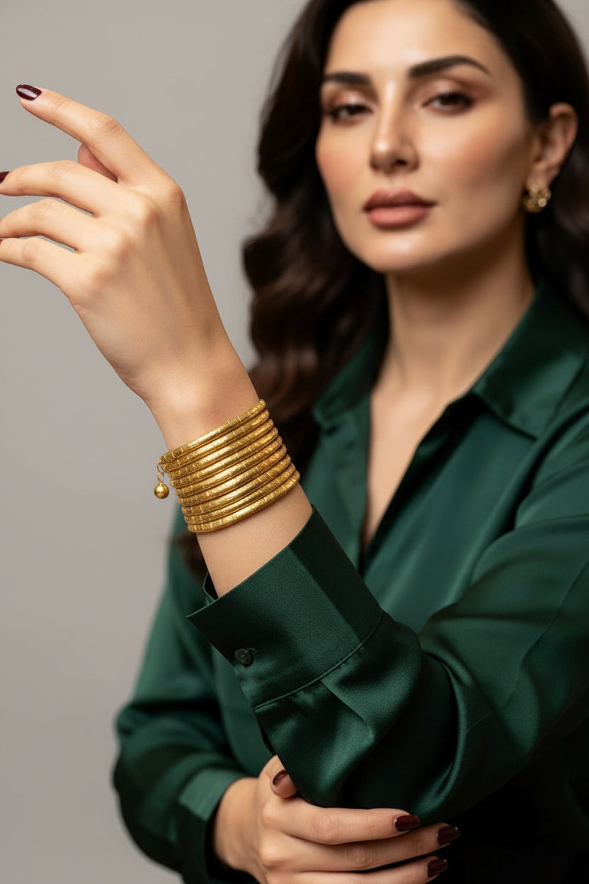 A model showcasing the Radha Gold-Tone Spiral Coil Cuff Bracelet by Famaza Couture, paired with a rich green silk blouse in a luxury jewelry boutique setting.