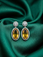 Pair of sterling silver two-tone gradient oval citrine drop earrings with diamond halos and round diamond studs on green satin.