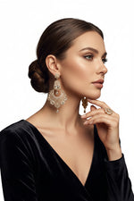 A sophisticated lifestyle photograph of a model in a black velvet dress, wearing ornate gold-toned chandelier earrings featuring intricate cubic zirconia craftsmanship, perfectly capturing a luxurious, high-fashion aesthetic.