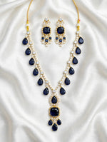 Sapphire blue pear & cushion-cut gemstone necklace with matching statement earrings, gold-tone finish with sparkling clear crystal accents — South Asian bridal & formal jewelry set on white silk background.