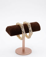 Two royal gold-plated AD kadas with side-lock mechanism displayed on a brown velvet jewelry stand.