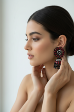 Model is wearing these earrings Rich black brass jhumka earrings adorned with a deep maroon floral stone stud and matching maroon stone embellishments.