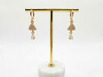Rose Gold earrings with dangling elements on a gold earring stand against a white background