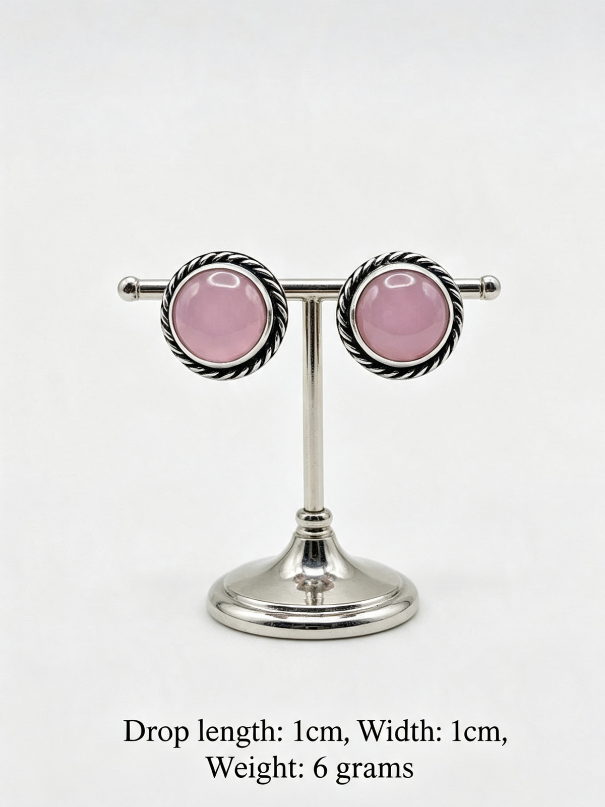 A pair of silver-toned drop earrings with oval pink gemstones, displayed on a silver stand against a white background, with text below showing dimensions and weight.