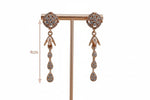 Rose gold earrings with gemstones on a stand against a grey background