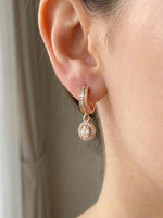 Rose gold hoop earring with a small round pendant worn by a model.