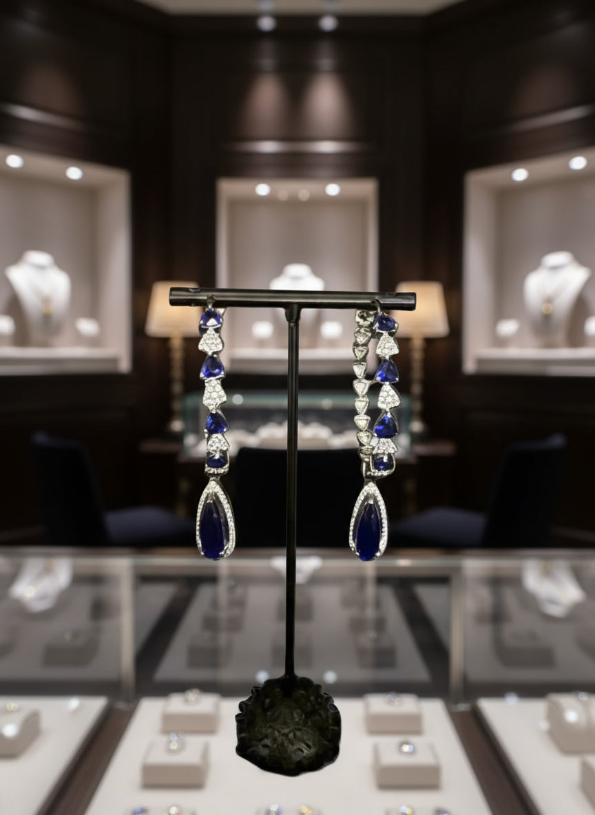 A pair of silver finish American diamond Jhumka bali earrings with green and clear stones on a stand.