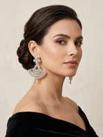 A pair of luxury ruby red and silver American Diamond fan-shaped chandelier earrings displayed on a T-bar stand, featuring a clover floral top stud, a central oval crimson stone, and an intricate flared skirt set with clear crystal baguettes.