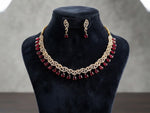 Gold-toned jewelry set displayed on a black velvet mannequin bust, featuring an ornate necklace with red teardrop stones and matching drop earrings.