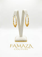 Pair of luxury gold-plated Bali hoop earrings featuring a crescent design with intricate gold bead drops, displayed on a posh white velvet stand for Famaza Couture.