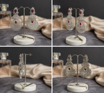 Luxury silver-tone chandelier earrings with ruby red stones displayed on a jewelry stand, featuring intricate filigree detailing and sparkling crystal accents.