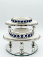 Pair of silver-plated hinged bangles featuring deep sapphire blue square stones and clear baguette-cut American Diamonds on a luxury display stand.