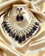 Luxury sapphire blue teardrop statement necklace and earring set, deep blue pear gemstones with brilliant CZ crystal accents, elegant presentation on champagne satin fabric, premium jewelry perfect for weddings and formal occasions.
