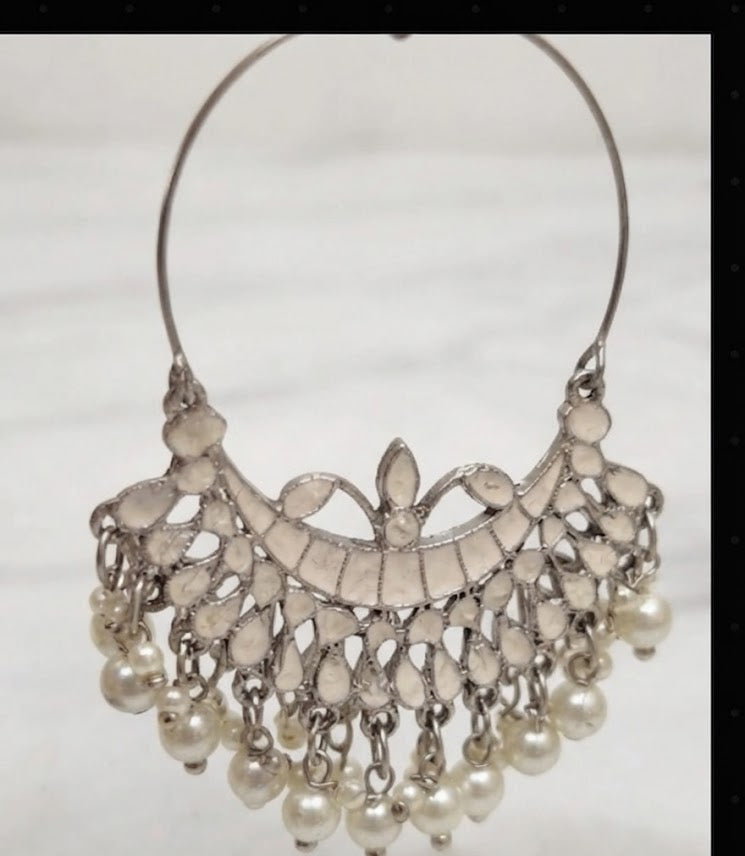 A pair of elegant, silver-toned Chaand Bali drop earrings with intricate lattice detailing and dangling pearl beads, displayed on a black velvet stand against a white marble background.