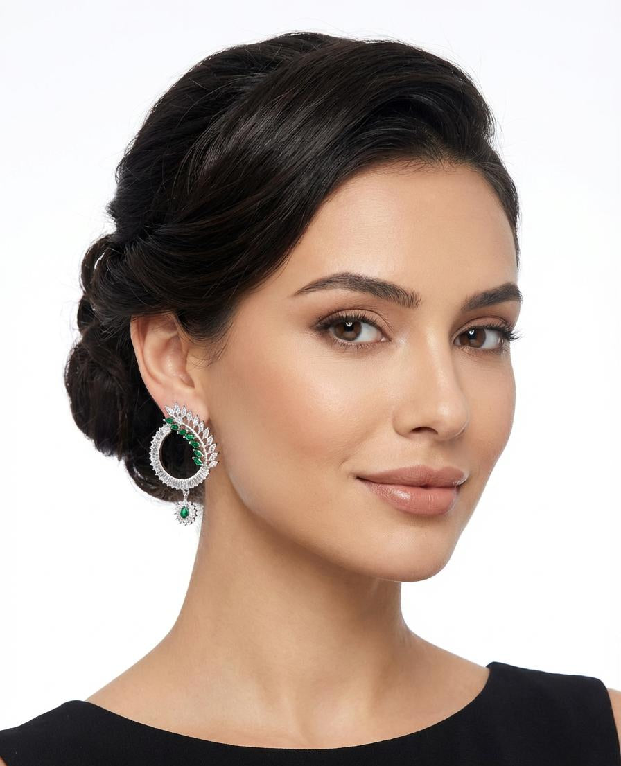 Silver-toned circular earrings featuring a curved line of emerald green marquise crystals and white baguette-cut stones.