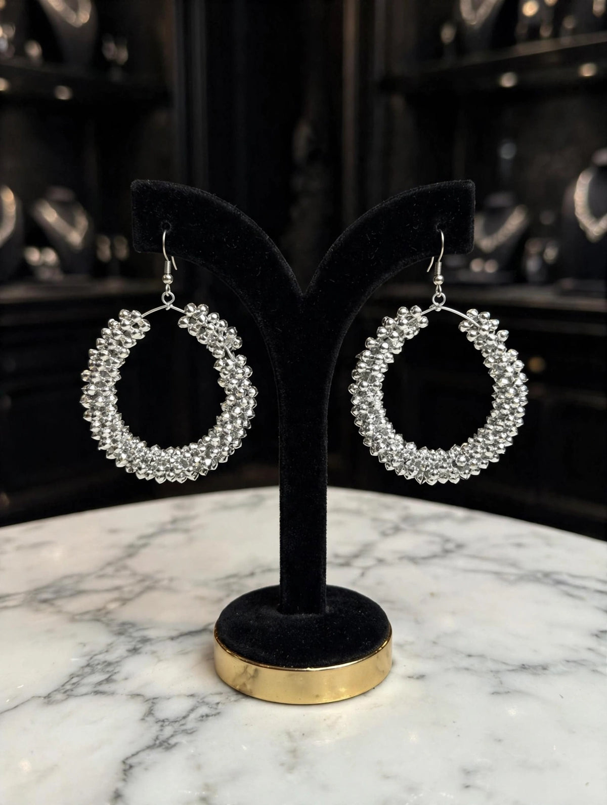 Pair of silver-tone crystal-encrusted teardrop hoop earrings on black velvet stand with gold base — Famaza Couture bridal luxury jewelry.