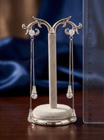 Silver earring stand with dangling earrings on a wooden surface, next to a ruler for scale.