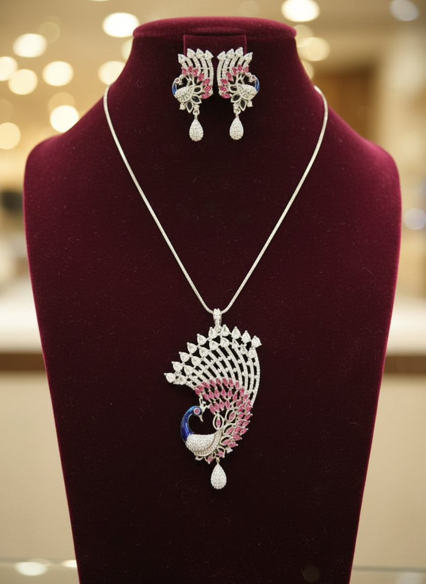 Silver plated a set of peacock-shaped pendant in silver chain with peacock-shaped earrings. The pendant is detailed with blue enamel and has sparkling crystal white AD and hot pink stones embellishments. Party wear jewellery set. Jewellery set is displayed on a black velvet jewellery dummy. Party wear set.