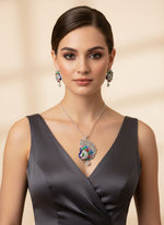 Silver polished a peacock full open wings design pendant with vibrant green, blue, red and pink enamel accents, along with white ad stones sparkling embellishments, accompanied by matching earrings, displayed on a black mannequin necklace stand. Party wear jewellery set.