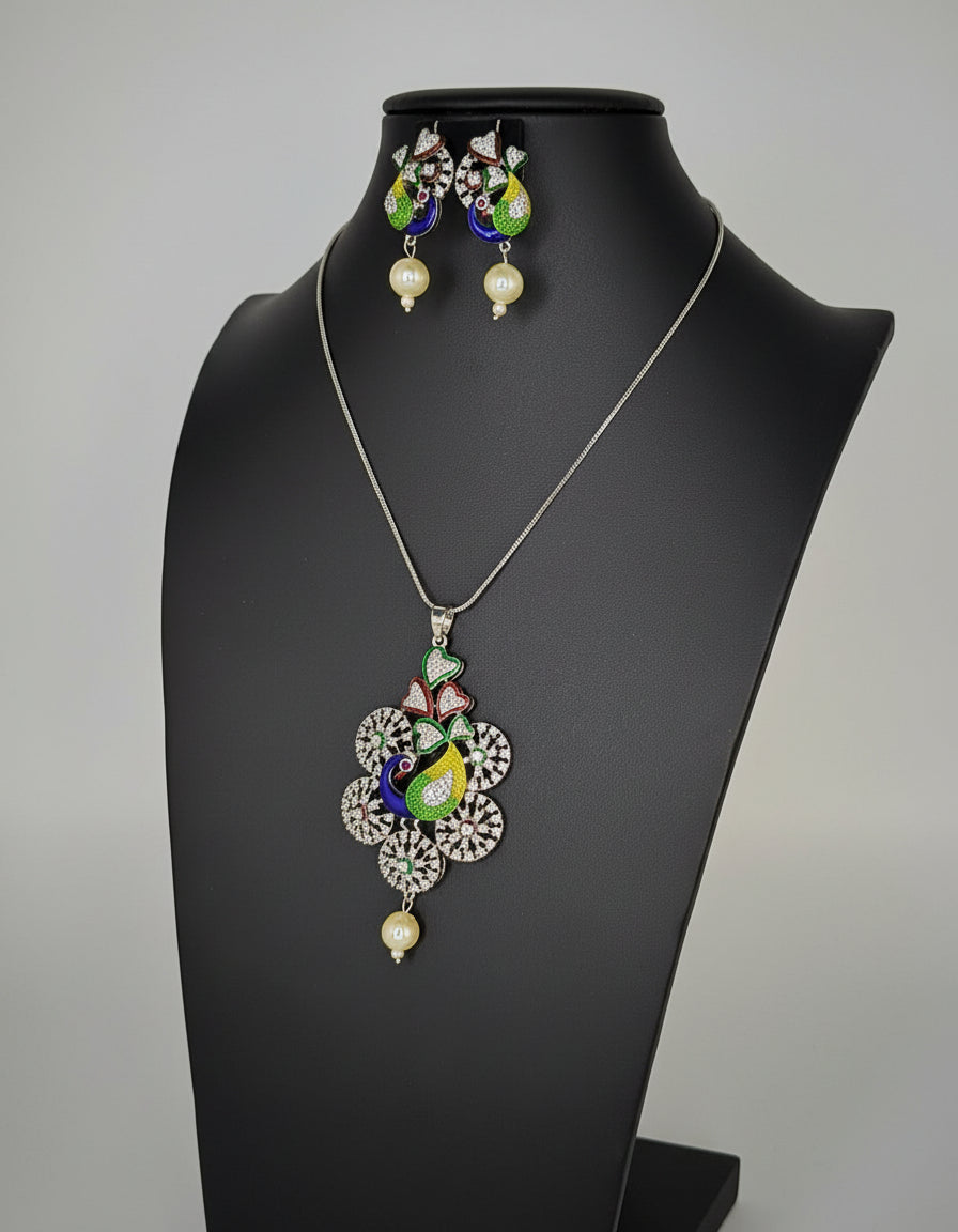 Silver polished a peacock pendant with vibrant green, blue, and gold enamel accents, along with sparkling embellishments, accompanied by matching earrings, displayed on a black mannequin necklace stand.