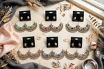 Six pairs of oxidised-look peacock chandbali earrings with ghungroo fringe, shown in green, red, black, orange, blue and white