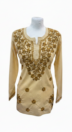 Creamy beige cotton short kurti featuring intricate dark yellow-brown floral embroidery along the neckline and scattered motifs across the front, displayed on a mannequin.