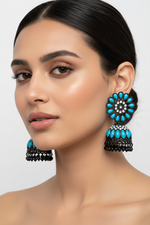 Model is wearing Stylish black brass jhumka earrings featuring a bold blue floral stone stud and matching blue stone accents on the jhumka base.