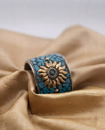 A wide, decorative cuff bracelet featuring a golden sunburst emblem amidst blue turquoise mosaic pieces, elegantly displayed on folds of shimmering beige silk fabric, with a vertical graphic indicating a product width of 4.5 cm.