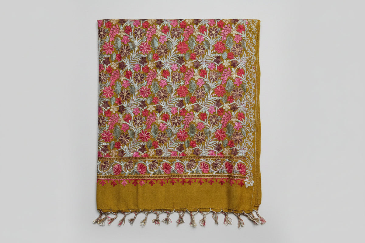 The Kashmiri embroidered pashmina scarf in mustard yellow with floral patterns and tassels on the ends.