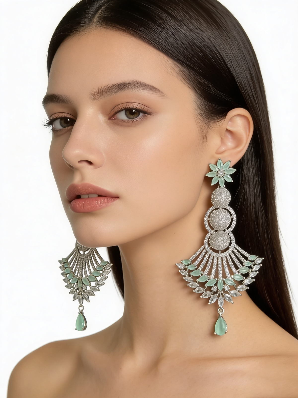 Model showcasing statement silver chaand bali earrings with mint green stones and clear crystal accents against a crisp white background.