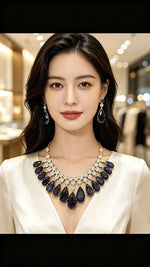 A woman with dark hair is wearing a luxurious teardrop necklace and matching drop earrings. The necklace features deep navy blue teardrop-shaped stones set in gold with clear crystal accents.