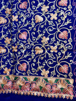 The blue Kashmiri embroidered pashmina scarf with maple leaf motifs and tassels on the ends, displayed on a wooden surface.