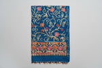 The blue Kashmiri embroidered pashmina scarf with tassels hanging at the ends, displayed on a wooden surface.