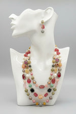 A gold-plated Kundan-studded and pearl-beaded handcrafted jewellery set, consisting of a necklace and earrings, displayed against a black background.