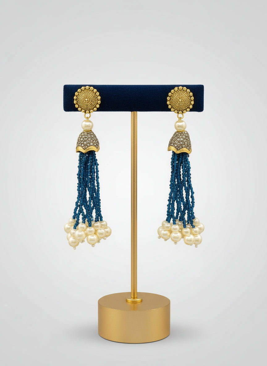 The gold-plated Kundan-studded and pearl-navy blue beaded handcrafted earrings, displayed against a black background.
