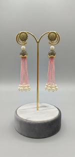 The gold-plated Kundan-studded and pearl-pink colour beaded handcrafted earrings, displayed against a black background.