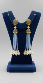 The gold-plated Kundan-studded and pearl-sky blue beaded handcrafted earrings, displayed against a black background.
