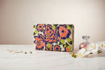 The handcrafted clutch bag with a floral pattern of glass beads on a light base fabric, displayed on a dark background.