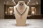 The mannequin showcasing a necklace set with navy blue and white ad stones, accompanied by earrings and a maang tikka.