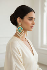 A pair of gold-plated Parul Pearl kundun earrings with intricate designs and drop-shaped pearls, displayed on a stand.