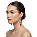 The pair of silver finish American diamond Jhumka bali earrings with green and clear stones on a stand.