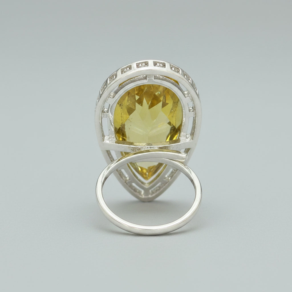 The rear view of a silver-toned ring with a teardrop-shaped yellow gemstone, displayed on a dark textured surface.