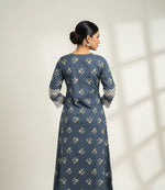 The rear view of a state blue long-sleeve kurta with a beige floral pattern and white lace trim on the cuffs and hem, laid flat on a light wood floor.