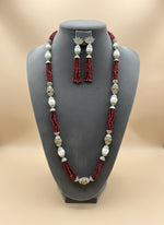 The set of jewellery featuring a long necklace with Red-coloured glass beads and metallic accents, paired with matching earrings, displayed on a mannequin bust.