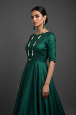 The set of jewellery featuring a long necklace with bottle green-coloured glass beads and metallic accents, paired with matching earrings, displayed on a mannequin bust. Party wear set.